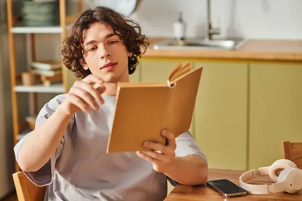 A handsome young man sits at a wooden table, focused on a book in a contemporary office setting. — Stock Photo