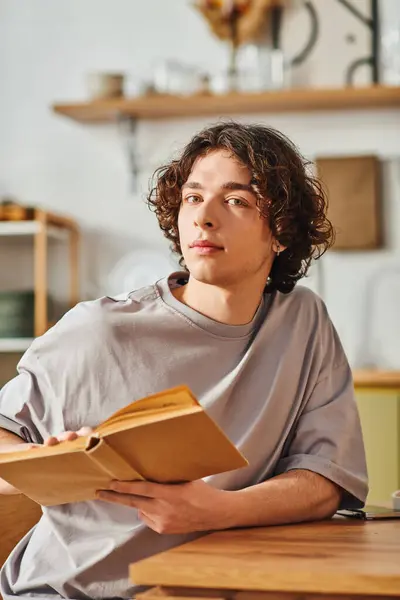 A young attractive man sits at a desk, engaged in reading a book, emanating a calm focus. — Stock Photo