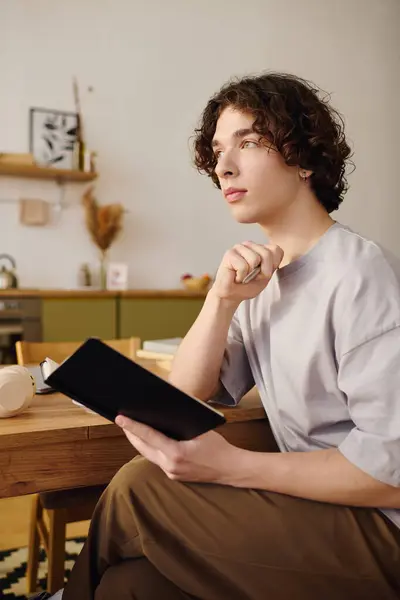 Young man with curly hair is pondering over notes while seated at a stylish desk in an office. — Stock Photo