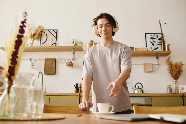 A young handsome man in a stylish office setting prepares a warm drink while wearing headphones. — Stock Photo