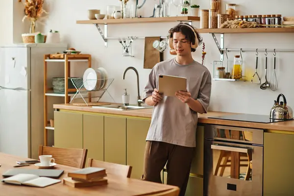 Engaging young man stands in a stylish office kitchen, focused on his tablet and enjoying his work. — Stock Photo
