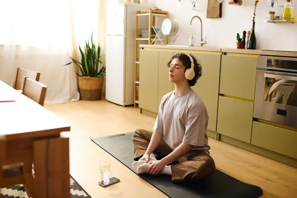 Un joven medita con las piernas cruzadas sobre una esterilla de yoga en una oficina de moda. - foto de stock
