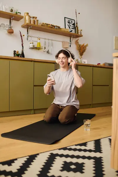 Relaxing in a stylish office, a young man listens to music and uses his phone while on a mat. — Stock Photo