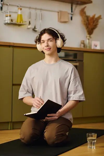 Handsome young man kneeling on yoga mat in office, jotting down ideas with focused expression. — Stock Photo