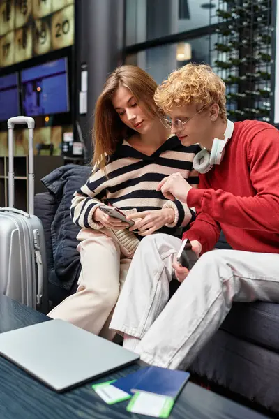 Una pareja de enamorados se relaja juntos en el vestíbulo de un hotel, compartiendo un momento mientras revisan sus teléfonos. - foto de stock