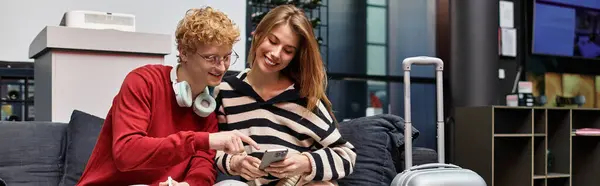 Una joven pareja comparte un momento alegre juntos en el vestíbulo de un hotel mientras mira su teléfono inteligente. - foto de stock