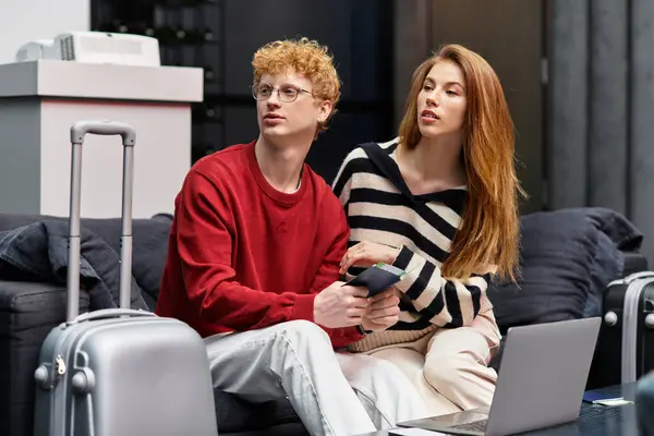 Couple relaxes on a plush sofa, sharing travel plans in their modern hotel room. — Stock Photo