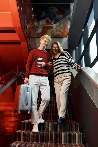 Una feliz pareja baja por las escaleras del hotel, disfrutando de la compañía de los demás. - foto de stock