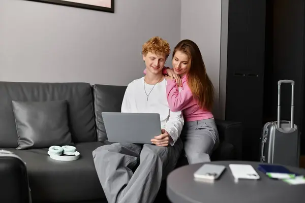 A young couple cuddles on a couch, sharing a laptop in their stylish hotel room. — Stock Photo