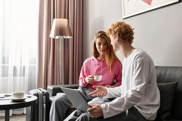 A young couple relaxes in a cozy hotel room, sharing smiles and warm drinks while connecting. — Stock Photo