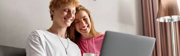 Young couple enjoying quality time, smiling and bonding over a laptop in a hotel setting. — Stock Photo