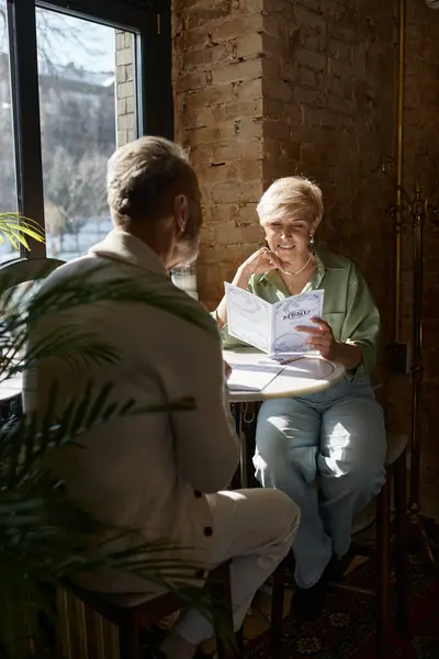 A middle-aged couple sits captivated at a cafe, sharing laughter while reading the menu. — Stock Photo