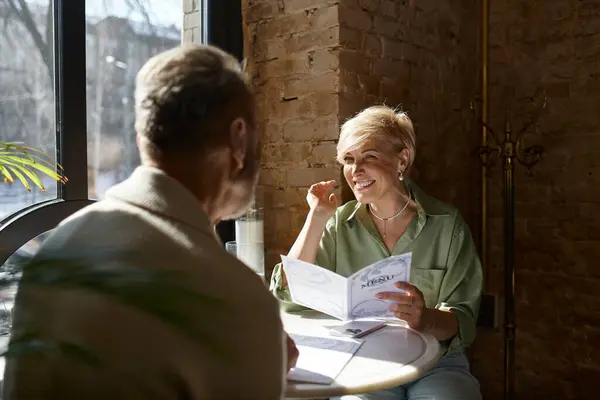 In a warm cafe, a middle aged couple shares laughter as they browse the menu. — Stock Photo