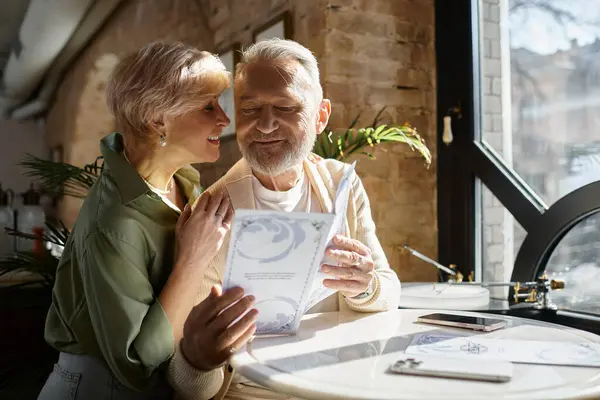 Middle aged man and woman share a warm moment over coffee while looking at a menu. — Stock Photo
