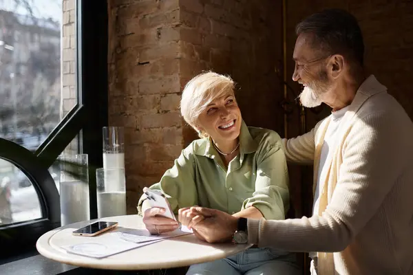 A middle aged couple shares smiles and laughter over coffee at a warm cafe setting. — Stock Photo
