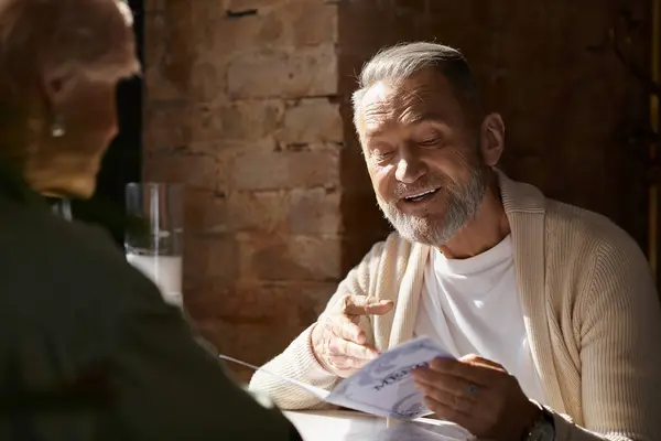 A middle aged man shares a light moment with his partner as they browse the menu together. — Stock Photo