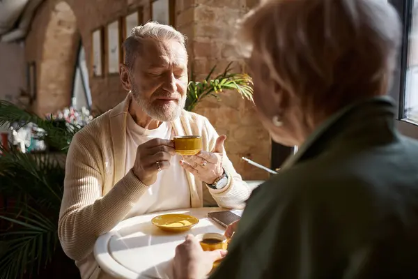 A middle aged man and woman share an intimate moment over coffee at a cozy cafe, basking in romance. — Stock Photo