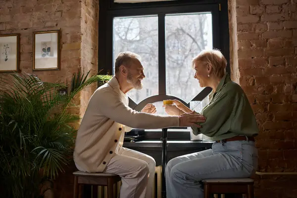 A middle-aged couple shares laughter and drinks, enjoying their intimate time by the window. — Stock Photo