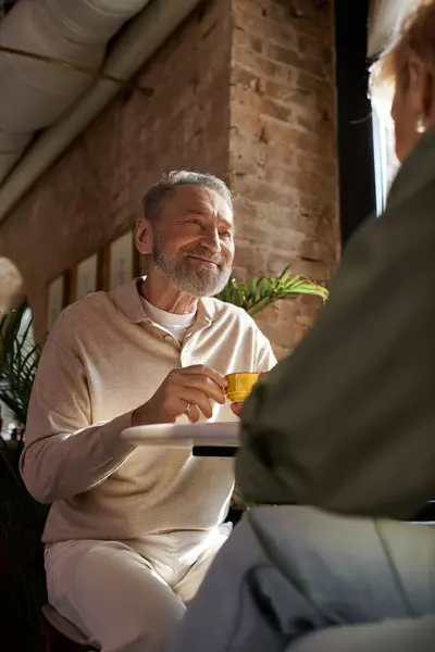 Ein Paar mittleren Alters teilt Lächeln und Gespräche bei Drinks in einem warmen Café-Ambiente. — Stockfoto