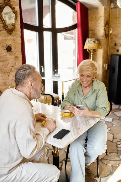 Two middle-aged people share coffee and enjoy each others company while on their smartphones. — Stock Photo