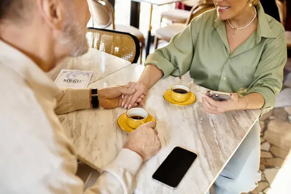 A mature couple shares a tender moment while sipping coffee and holding hands at a cafe — Stock Photo