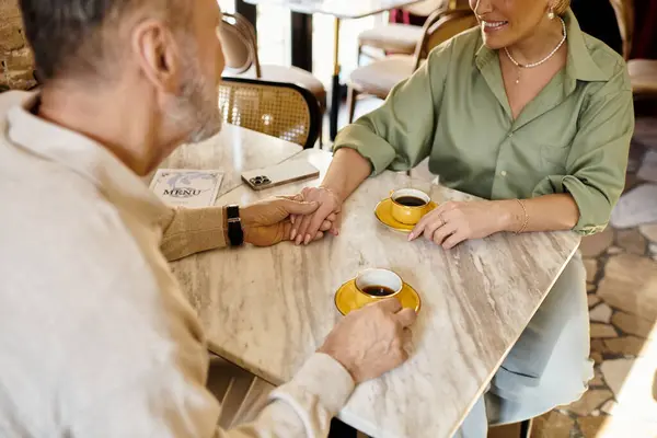 A lovely couple shares a warm moment over coffee, hands intertwined, amidst cafe ambiance. — Stock Photo