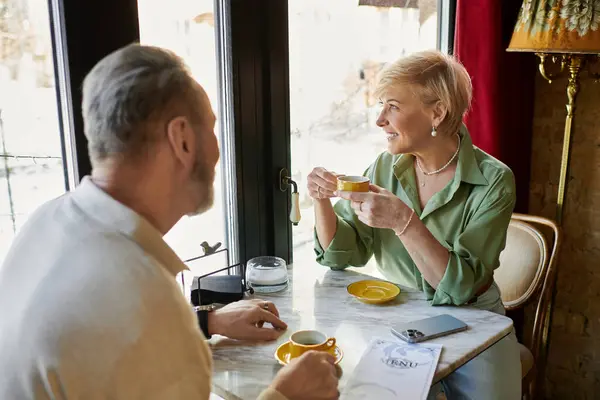 A middle aged man and woman share a warm moment at a cafe, sipping coffee and smiling. — Stock Photo