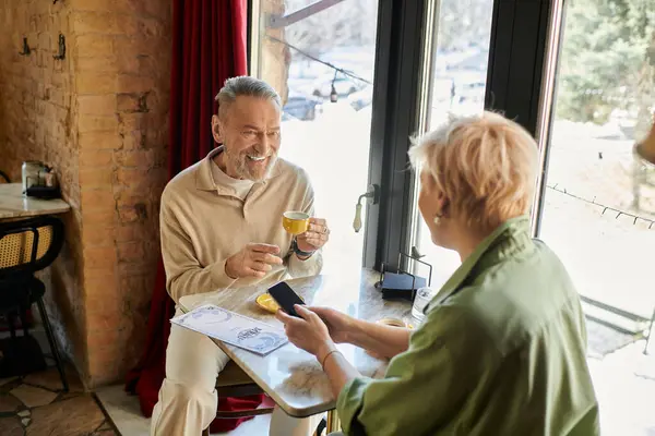A middle aged man and woman savor coffee while sharing smiles and conversation in a warm cafe. — Stock Photo