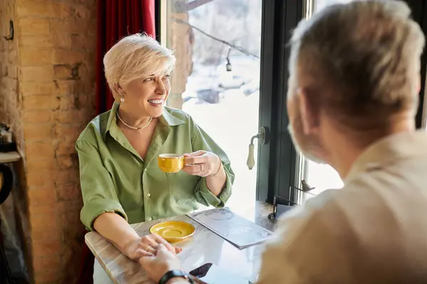 A middle aged couple smiles at each other while sipping tea in a quaint cafe on a sunny day. — Stock Photo