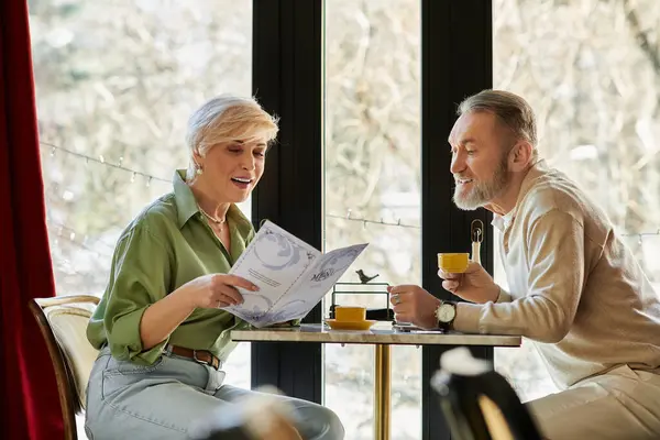 A couple engages in a delightful conversation while examining the menu in a serene cafe. — Stock Photo