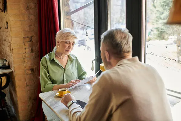 Paar mittleren Alters genießt ein herzliches Gespräch bei Kaffee beim gemeinsamen Lesen der Speisekarte. — Stockfoto