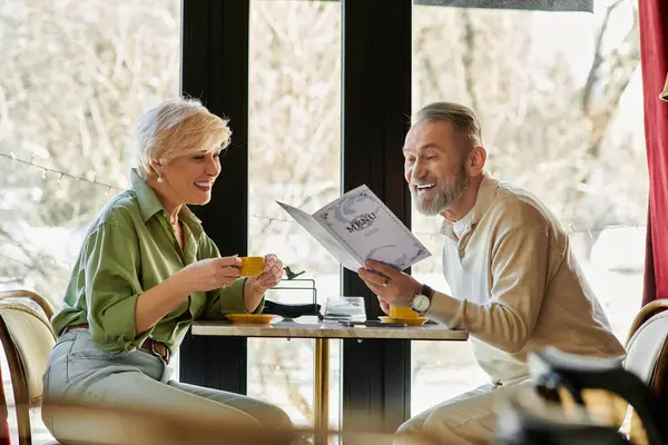Ein nettes Paar reifer Erwachsener lächelt und unterhält sich bei Kaffee, während sie die Speisekarte durchlesen. — Stockfoto