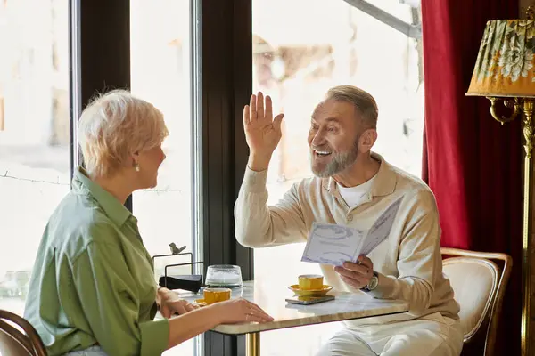 A middle aged man shares a joyful moment with his partner during their cafe date. — Stock Photo