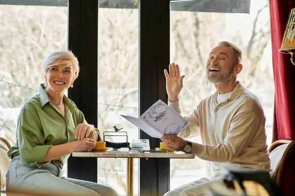 A middle-aged couple shares laughter and joy while waving to waiter in cafe — Stock Photo