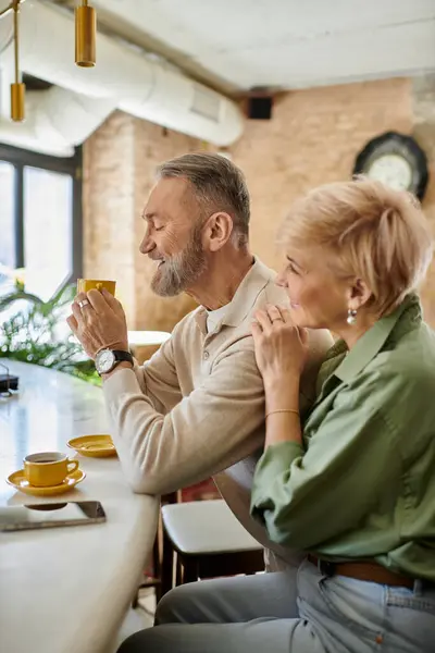 Ein Paar mittleren Alters teilt einen herrlichen Moment, nippt am Kaffee und lacht zusammen. — Stockfoto
