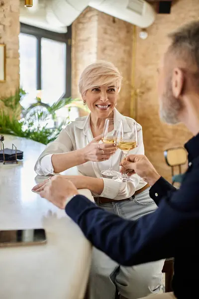 A middle aged man and woman share a joyful toast, enjoying their time together at a quaint cafe. — Stock Photo