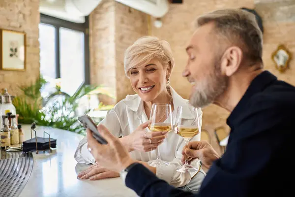 A mature couple shares a toast with drinks while laughing, sitting at a charming bar. — Stock Photo