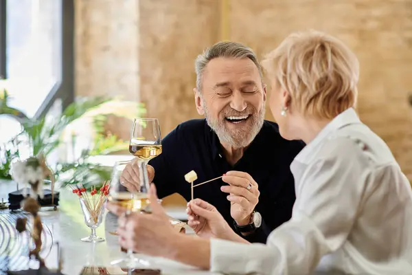 Middle aged couple shares laughter and delicious snacks over drinks in an intimate setting. — Stock Photo