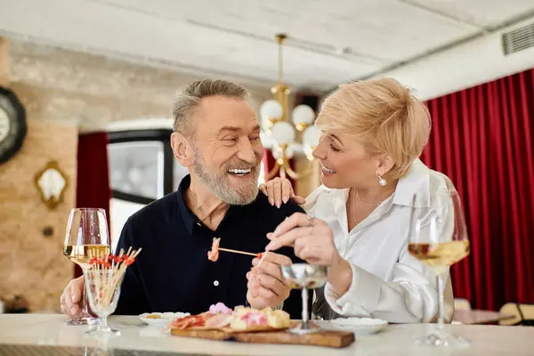 A middle-aged man and woman share laughter and delicious food during a romantic evening together. — Stock Photo