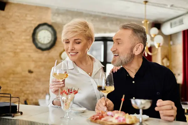 A middle-aged couple shares laughter and wine while indulging in delicious appetizers together. — Stock Photo