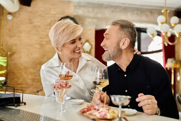 Middle aged couple shares laughter and wine while savoring delicious bites on their date night. — Stock Photo