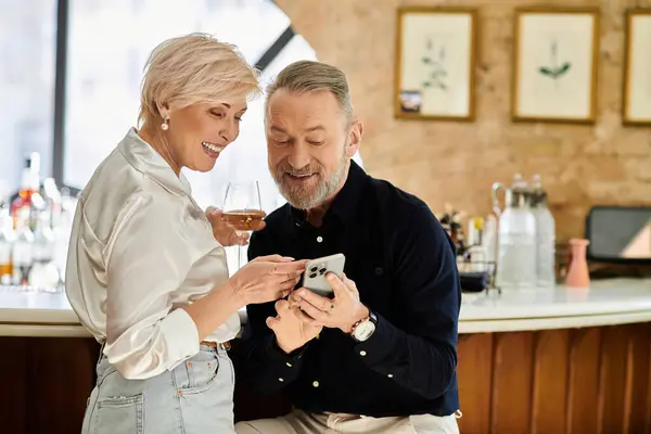 Paar mittleren Alters lächelt und lacht, während es einen Moment bei Drinks an einer Bar teilt. — Stockfoto