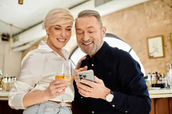 Ein Paar mittleren Alters lacht beim Anblick eines Telefons und genießt sein Date mit Drinks. — Stockfoto