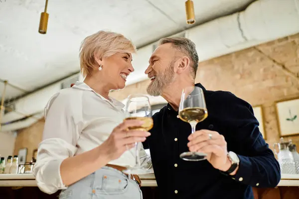 Ein Paar mittleren Alters lächelt liebevoll, während es zur Feier ein Glas Wein in die Höhe hält. — Stockfoto