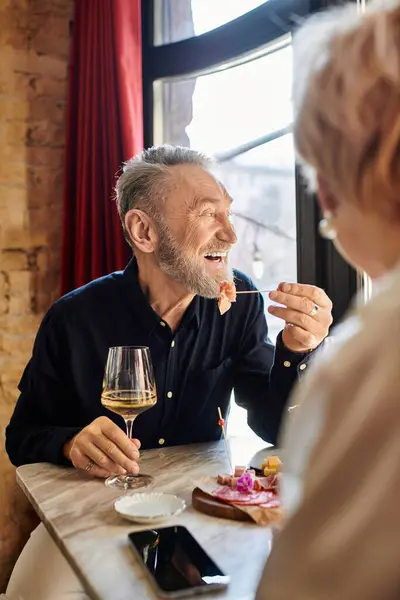 Um alegre casal de meia-idade desfruta de sua data, rindo sobre comida saborosa e bebidas. — Fotografia de Stock