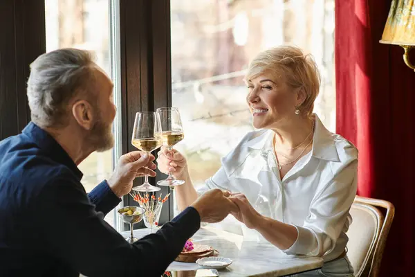 Um casal de meia-idade brinda juntos, sorrindo e desfrutando de seu tempo na mesa. — Fotografia de Stock