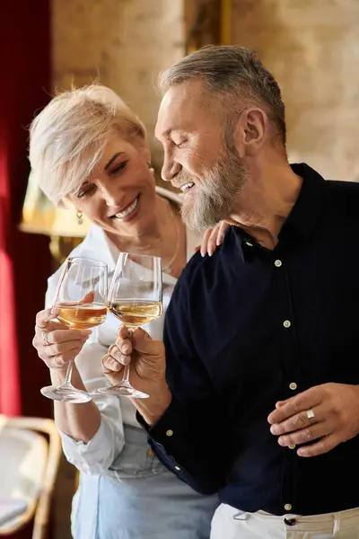 Middle aged couple enjoys a romantic evening, toasting with glasses of white wine in a warm setting. — Stock Photo