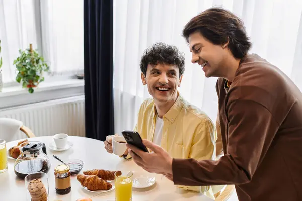 Two handsome men enjoy breakfast together, sharing smiles and laughter in their stylish kitchen. — Stock Photo