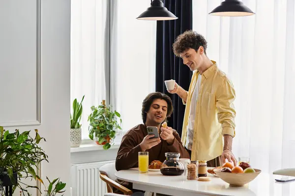 Two good looking men enjoy a sunny morning in their chic apartment, sharing smiles and drinks. — Stock Photo