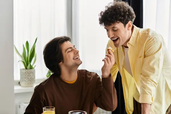 Two men enjoy a playful moment together while sharing a snack in their stylish apartment. — Stock Photo